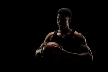 Basketball player holding a ball against black background. Screaming african american man...