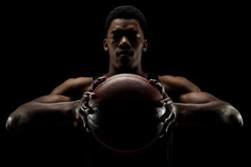 Fototapeta na wymiar Basketball player holding a ball against black background. Serious concentrated african american man.