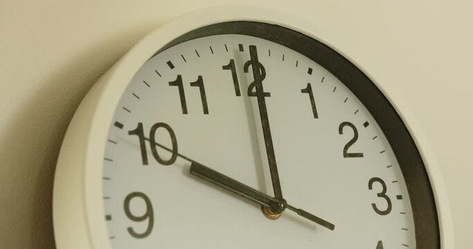 close-up of a white wall clock showing the time 10:00. the seconds hand moves slowly