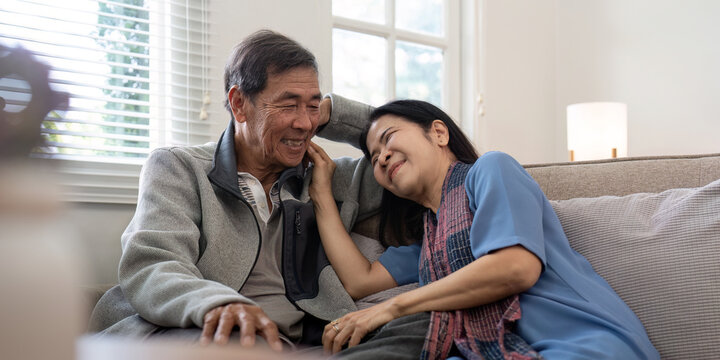 Happy mature husband and wife sit rest on comfortable sofa in living room enjoy talking, smiling elderly couple relax on couch at home chat speak laugh on leisure weekend