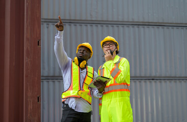Portrait of African male engineer and Asian worker wearing safety helmet and reflective vest working together in container yard. Dock worker and supervisor checking containers data
- 748671336