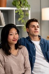 Smiling young adult diverse couple relaxing together on sofa at home. Woman looking at camera next to a happy man sitting on a couch in the living room.