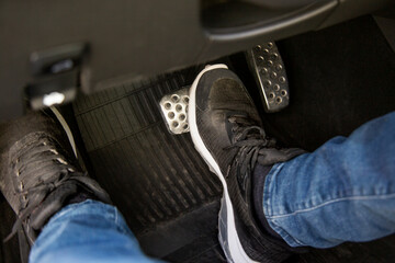 man's feet in black sneakers on the floor in a car pushing down the brake pedal, carefully driving...