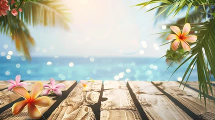 Zelfklevend Fotobehang An empty wooden desk adorned with plumeria flowers and palm leaves sits against an ocean backdrop, illuminated by bokeh sunlight. Background for displaying summer and tropical beach products. © Bnz