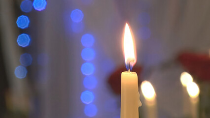 A candle is burning on the background of a garland.