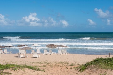 Fototapeta na wymiar Porto de Galinhas Beach, Pernambuco, Brazil. Chairs and umbrellas on the sand, blue and turquoise sea, horizon and blue sky.