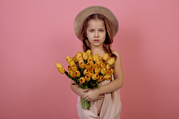 Little girl with pigtails holding flowers wearing hat on pink background. International women's day.