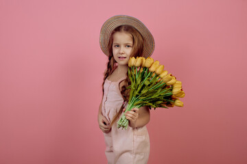 Little girl with pigtails holding flowers wearing hat on pink background. International women's day.