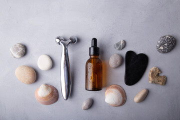 beauty essentials and facial massage tools among pebbles on a grey backdrop. Summer spa care concept