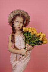 Little girl with pigtails holding flowers wearing hat on pink background. International women's day.