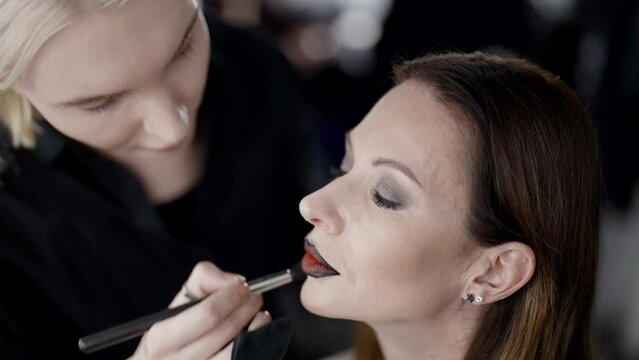 beautiful middle-aged woman in beauty studio, male makeup artist applying foundation on female face
