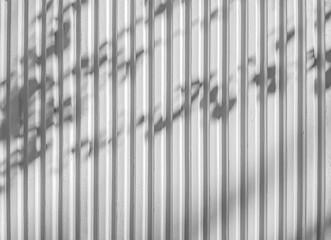 Obraz premium Fondo abstracto con un patrón vertical en una pared metálica con sombras de las hojas de los árboles, en blanco y negro