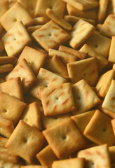 A lot of small cookies are square shaped. A pattern of a yellow salt cracker. Background image with salted pastry.