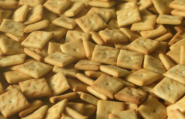 A lot of small cookies are square shaped. A pattern of a yellow salt cracker. Background image with salted pastry.