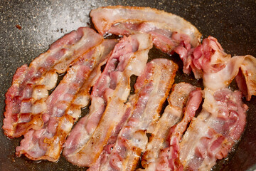 slices of bacon fried in a pan on the stove