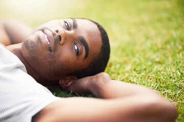 Portrait, relax and black man on grass in garden of summer home for peace, wellness or mindfulness. Face, nature and field with happy young person lying on green ground from above for break or rest