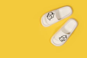 A pair of beige rubber slippers with cat on a yellow background. Fashionable rubber slippers