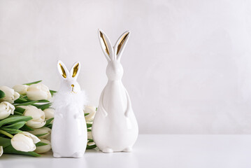Two Easter rabbits figurines with bouquet of white tulips on white background. Easter celebration...