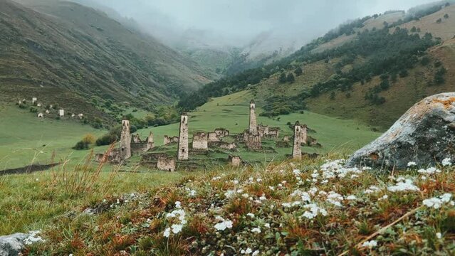 View of the medieval Targim tower complex in the Caucasus mountains surrounded by greenery. The Caucasus Mountains on a cloudy day in Ingushetia. Russia, 4K.