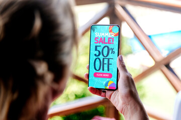 Summer sale offer Ad. Up to 50% off. Woman holding a mobile phone showing an offer or coupon on the...