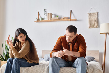 frustrated  multiethnic couple sitting and quarrelling in bedroom at home, divorce concept