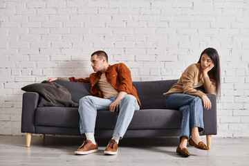young interracial couple with emotional distress sitting on couch in living room, divorce concept