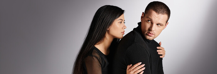 young and tender asian woman embracing gloomy and frustrated man on grey backdrop, horizontal banner