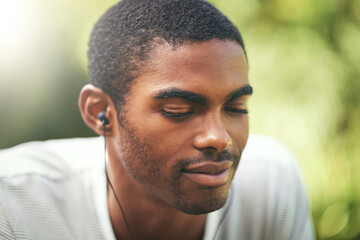 Face, music and relax with black man in nature or park outdoor for summer, peace and quiet. Garden, radio and wellness with calm young person streaming audio or sound on earphones in backyard