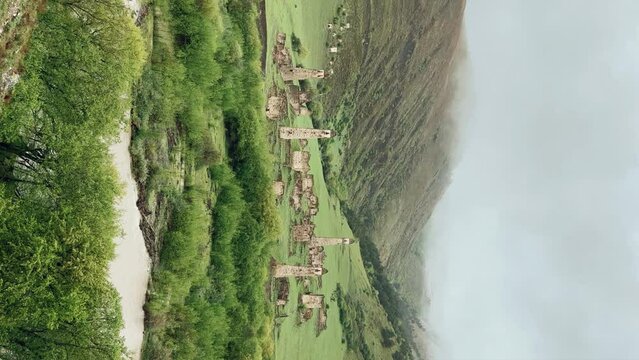 View of the medieval Targim tower complex in the Caucasus mountains surrounded by greenery. The Caucasus Mountains on a cloudy day in Ingushetia. Russia, 4K.