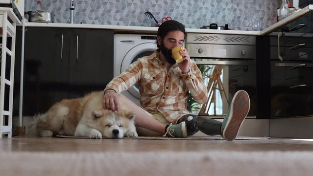 man with bionic leg, due to amputation, in his apartment, single with his dog sitting in the kitchen, while drinking coffee