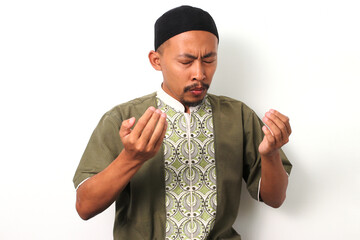 An Indonesian Muslim man in koko and peci prays with devotion during Ramadan, his open hands raised...