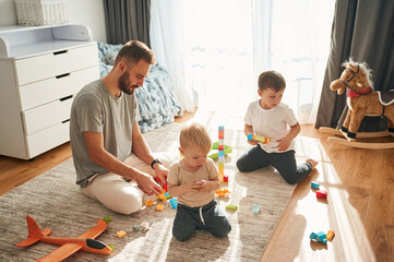 Father is playing with two little boys on the floor with toys
