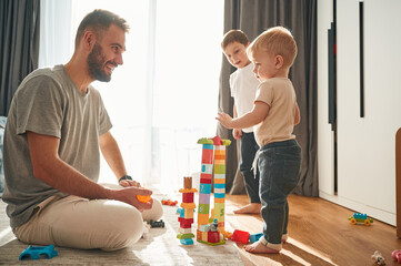 Father is playing with two little boys on the floor with toys