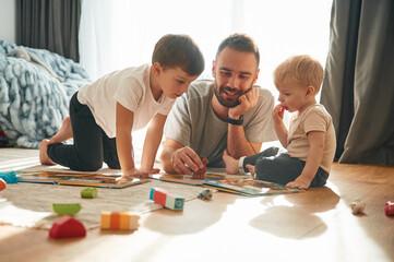 Lying down, board game. Father is playing with two little boys on the floor with toys
