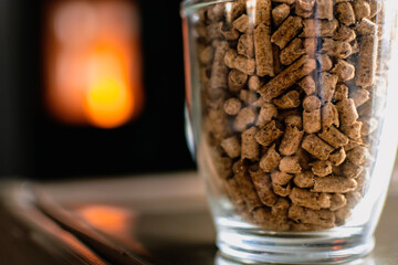 Pellet for stove or boiler in a glass, compressed wood pellet with a stove in background