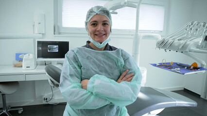 Portrait of a happy female Dentist at dental clinic with arms crossed representing healthcare professional workforce wearing uniform with equipment in background