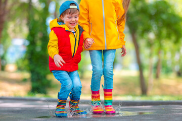 Happy kids girl and boy with umbrella and color rubber rain boots play outdoor and jump in dirty rainy puddles - 748732907