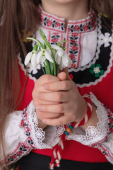 Bulgarian girl in traditional folklore costumes with spring flowers snowdrop and handcraft wool bracelet martenitsa symbol of Baba Marta - 748733135