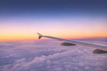 Airplane flying over color sky clouds during scenic sunset or sunrise cloudscape, view from plane window of wing turbines and horizon - 748733382