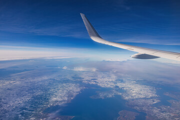 Airplane fly high in sky on a sunny day, view from plane window of clouds and wing turbines - 748733703