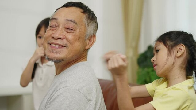 Footage handheld dolly shot, Joyful girl massage on Retirement grandfather's shoulder on sofa, Granddaughter has fun while take care her grandpa with love in living room at home