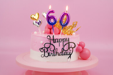 Birthday cake with golden crown and pink burning candles, numbers 60 on pink.
