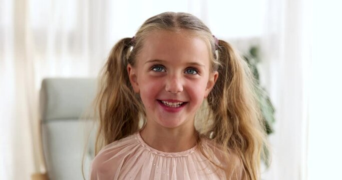 Smiling little girl of five years old looking at the camera and laughing with two ponytails in a pink dress close-up portrait standing at home. Child smiling looking up close up head shot