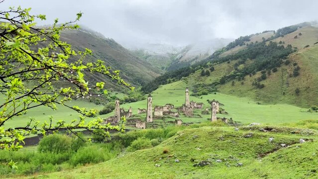 View of the medieval Targim tower complex in the Caucasus mountains surrounded by greenery. The Caucasus Mountains on a cloudy day in Ingushetia. Russia, 4K.
