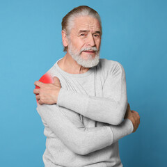 Senior man suffering from rheumatism on light blue background