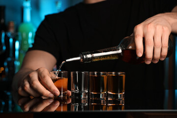 Bartender pouring alcohol drink into shot glass at mirror counter in bar, closeup