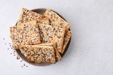 Cereal crackers with flax, sunflower and sesame seeds in bowl on light textured table, top view. Space for text