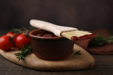 Marinade in bowl and basting brush on wooden table, closeup