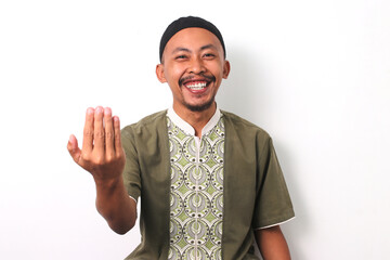 Indonesian Muslim man in koko shirt and peci smiles and extends a friendly hand gesture towards the...