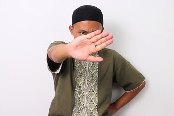 Indonesian Muslim man in koko shirt and peci crosses his arms in a stop gesture. Isolated on White...